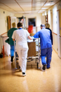 vårdpersonal som skjuter en vårdsäng genom korridoren.